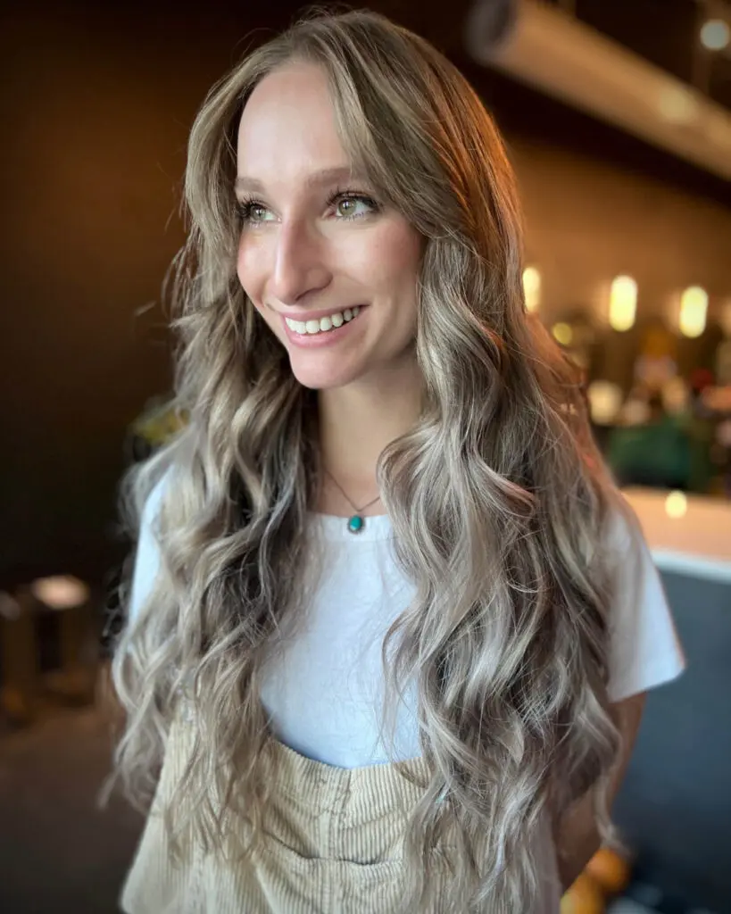 Ultra-Long Cool Ash Blonde Balayage with Cascading Beachy Waves Smiling client showcasing ultra-long cool ash blonde balayage hair with a shadow root and face-framing layers styled in cascading beachy waves at Sunday Salon in Raleigh, NC.