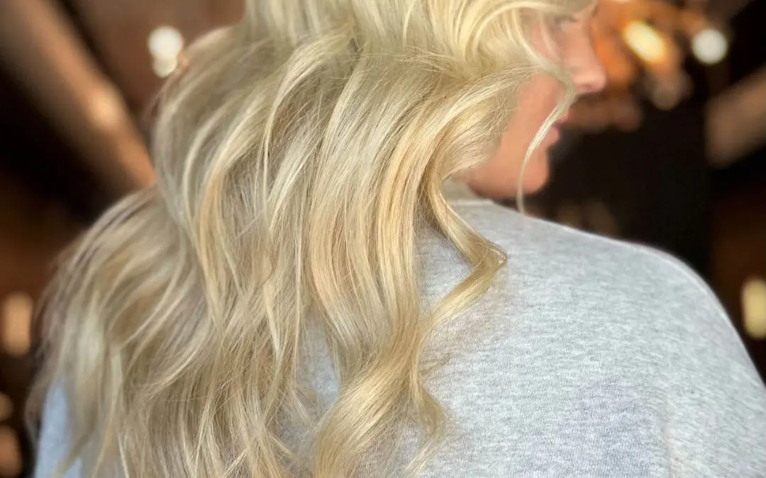 Back view of a client showcasing long, bright buttery blonde hair styled in cascading voluminous waves at Sunday Salon in Raleigh, NC.