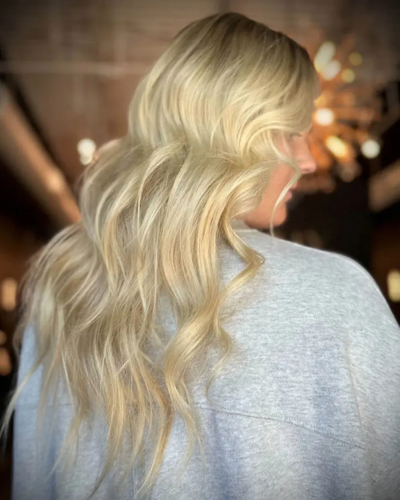 Back view of a client showcasing long, bright buttery blonde hair styled in cascading voluminous waves at Sunday Salon in Raleigh, NC.