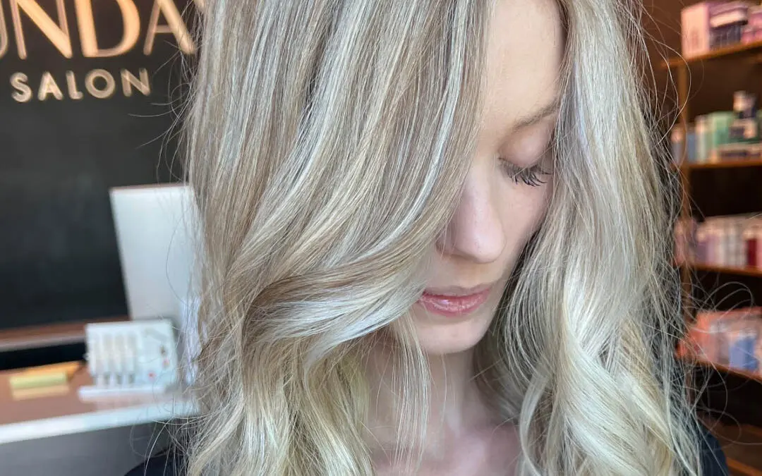 Close-up of a client with long, highly dimensional icy cream blonde highlights and a subtle shadow root, styled in sweeping voluminous waves at Sunday Salon in Raleigh, NC.