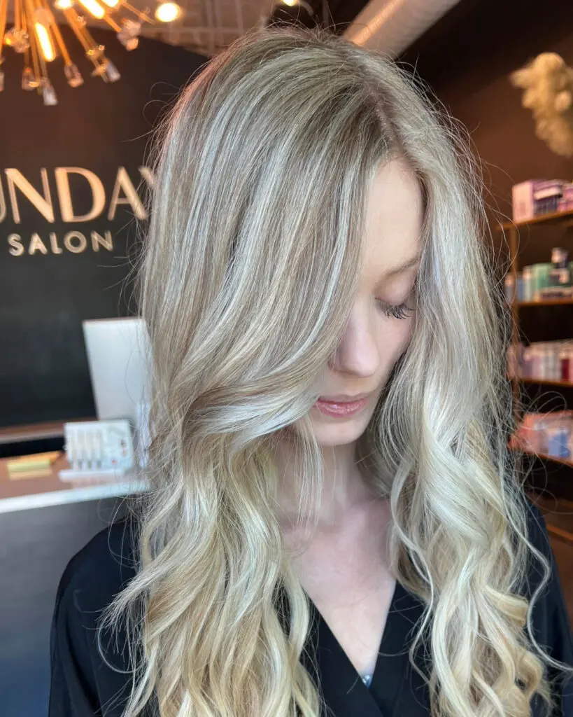 Close-up of a client with long, highly dimensional icy cream blonde highlights and a subtle shadow root, styled in sweeping voluminous waves at Sunday Salon in Raleigh, NC.