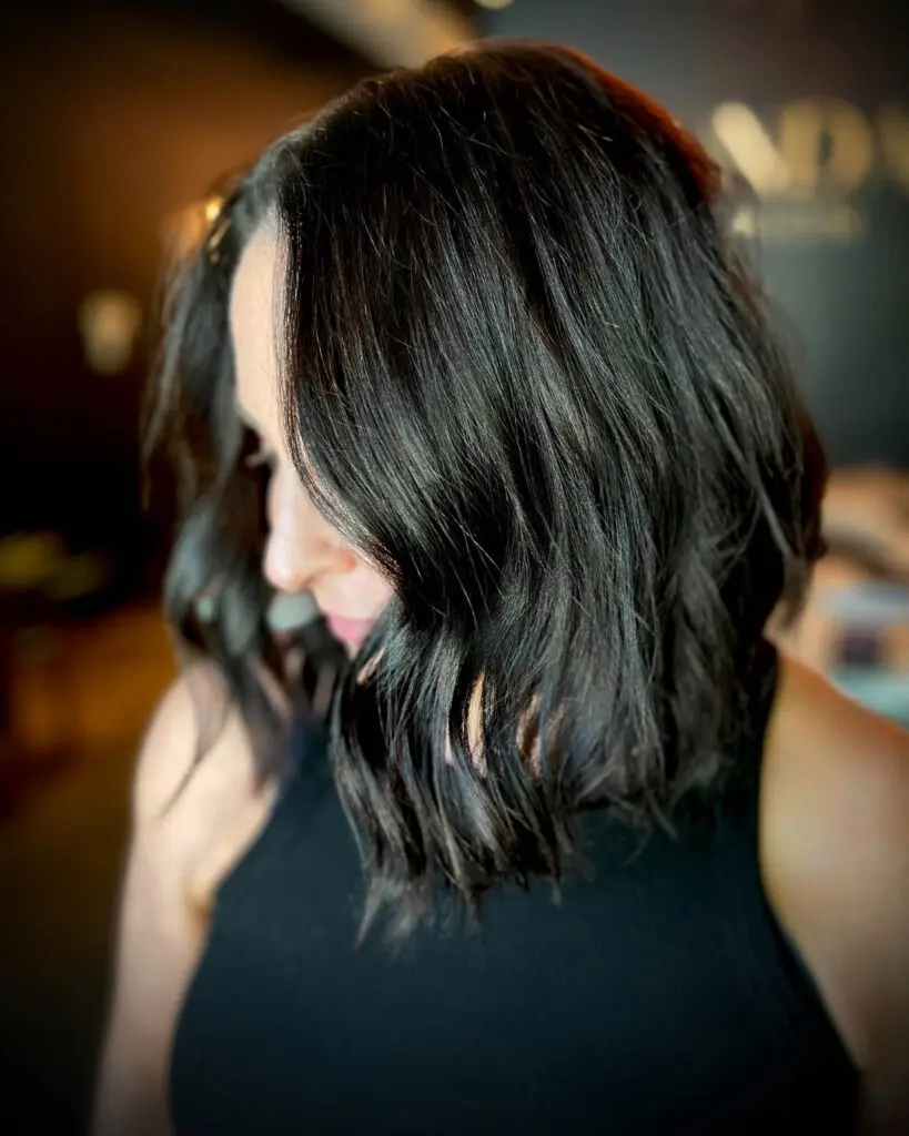 Side profile of a client showcasing a highly reflective, deep espresso collarbone-length textured lob styled in soft, undone waves at Sunday Salon in Raleigh, NC.