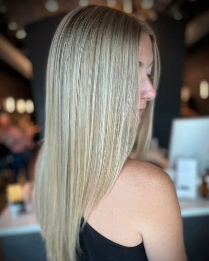 Back view of a client showcasing sleek, long, dimensional pale champagne blonde hair with a soft shadow root, styled perfectly straight at Sunday Salon in Raleigh, NC.