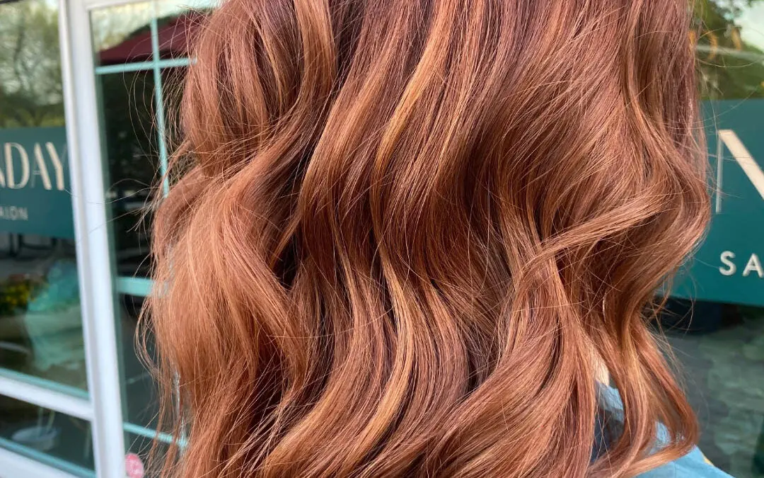 Close-up of a client showcasing vibrant dimensional copper red hair styled in soft cascading waves outside Sunday Salon in Raleigh, NC.