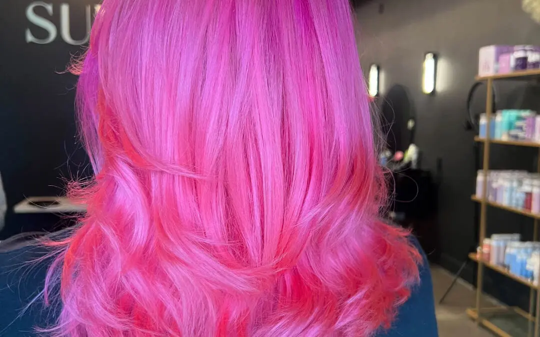 Back view of a client showcasing a vibrant, highly saturated neon pink hair color styled with bouncy, voluminous layered ends at Sunday Salon in Raleigh, NC.