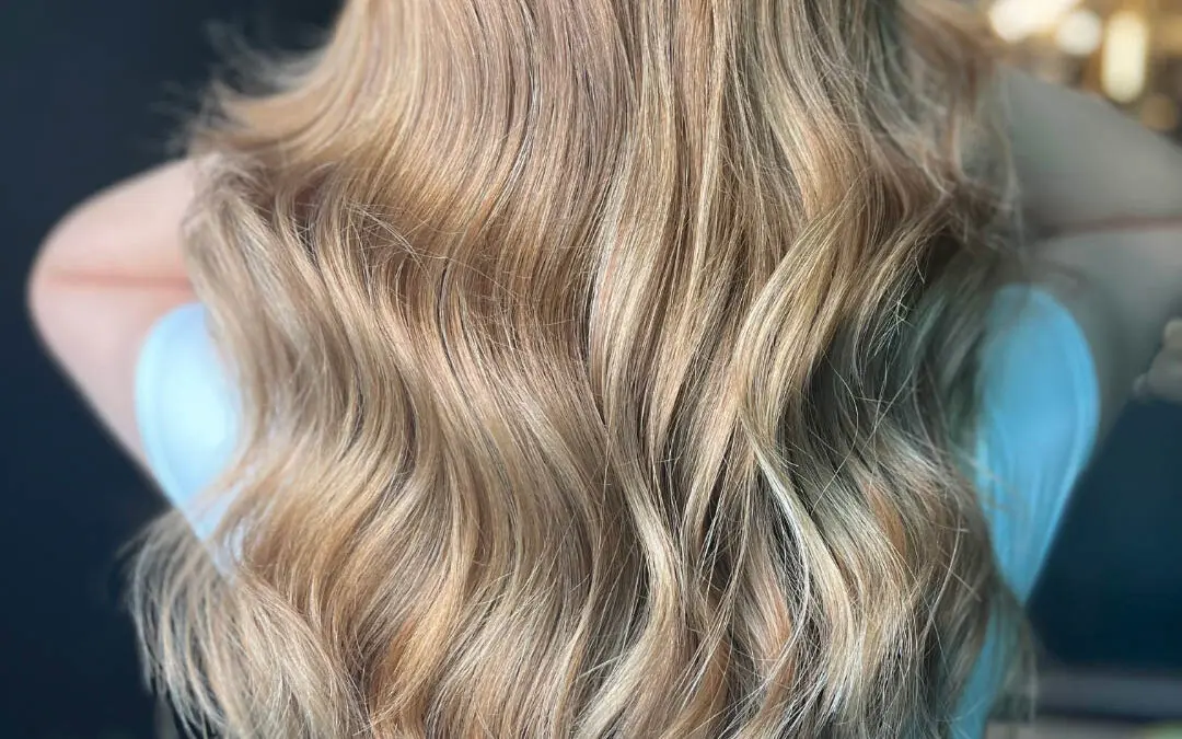 Back view of a client showcasing ultra-long, dimensional golden honey blonde balayage hair styled in soft cascading waves at Sunday Salon in Raleigh, NC.