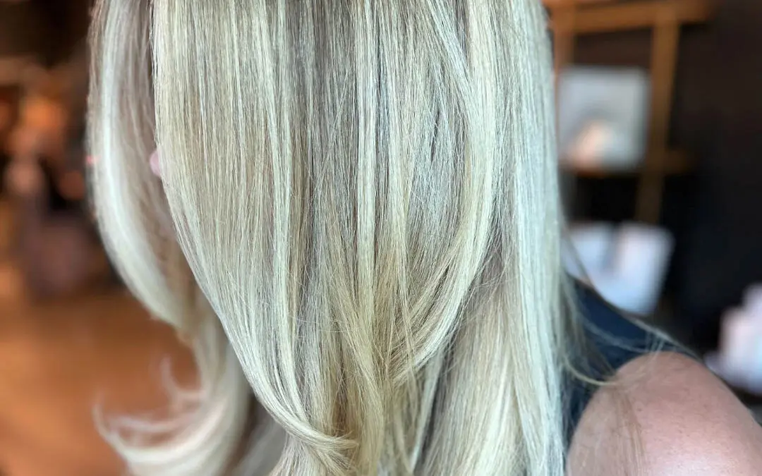 Side profile of a client showcasing long dimensional creamy vanilla blonde hair with a shadow root and sweeping face-framing layers, styled in a bouncy blowout at Sunday Salon in Raleigh, NC.