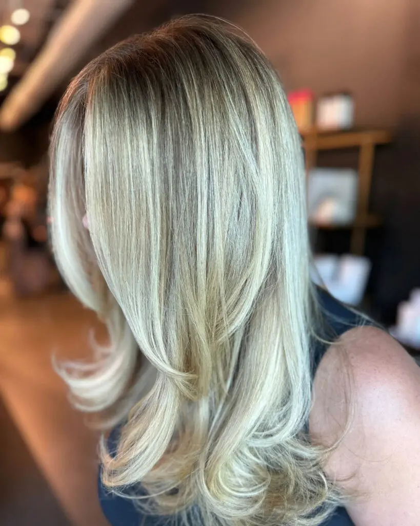 Dimensional Creamy Vanilla Blonde with Sweeping Layers and a Bouncy Blowout Side profile of a client showcasing long dimensional creamy vanilla blonde hair with a shadow root and sweeping face-framing layers, styled in a bouncy blowout at Sunday Salon in Raleigh, NC.