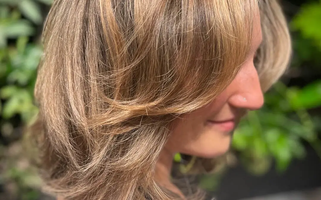 Back view of a client with defined, medium-length natural spiral curls featuring dimensional golden caramel highlights, styled to perfection at Sunday Salon in Raleigh, NC.