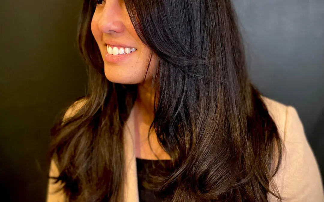 Smiling woman with ultra-long, rich espresso brunette hair styled in a voluminous blowout with sweeping face-framing layers, cut by Katherine Beingolea at Sunday Salon in Raleigh, NC.