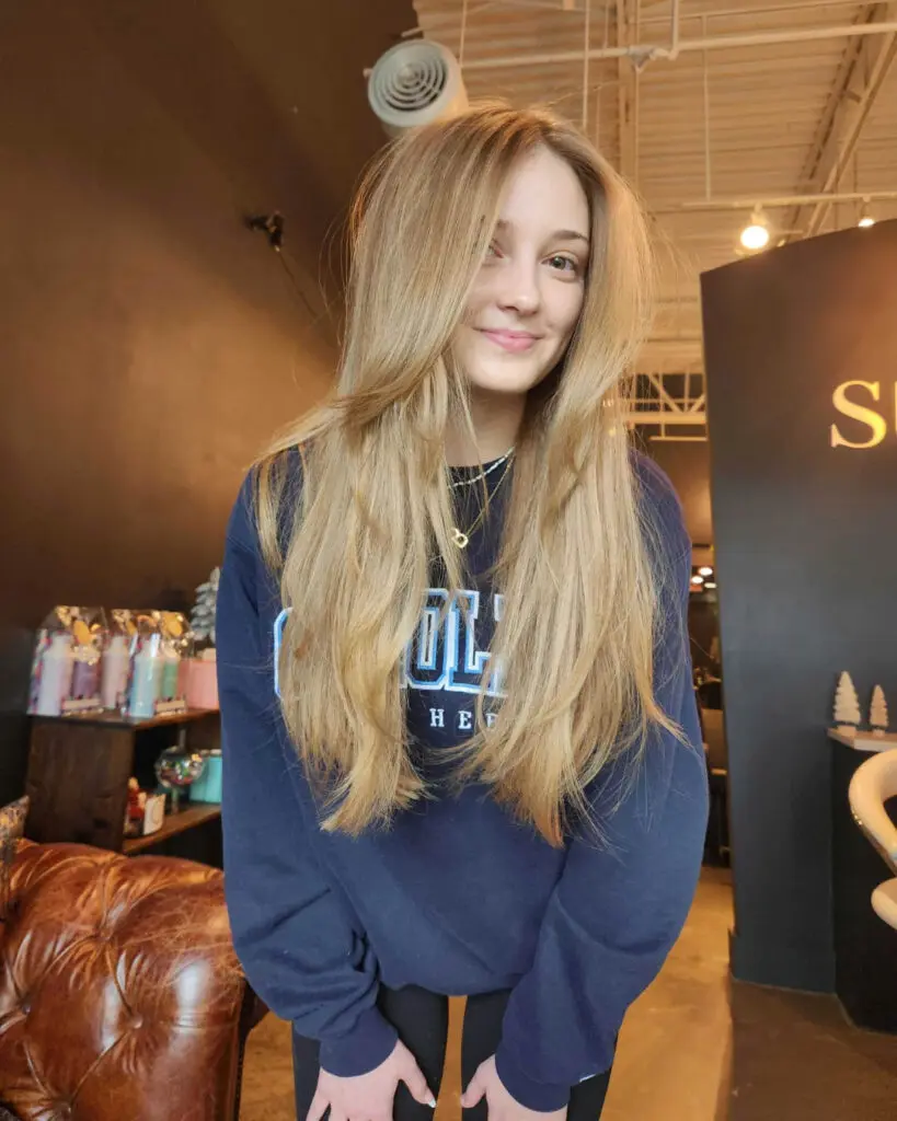A smiling client at Sunday Salon in Raleigh showcasing ultra-long, voluminous sandy blonde hair with seamless sweeping face-framing layers and a soft blowout.