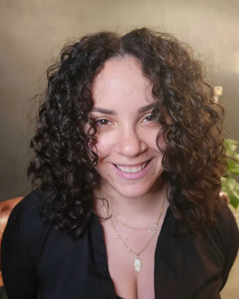 Smiling client at Sunday Salon in Raleigh showcasing a gorgeous shoulder-length curly haircut with perfectly defined, bouncy dark brunette ringlets.