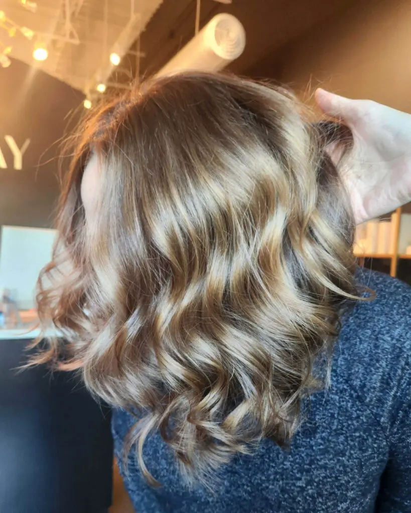Close-up of a client at Sunday Salon in Raleigh showcasing a fresh, shoulder-length lob haircut styled in bouncy waves with dimensional honey and caramel highlights.