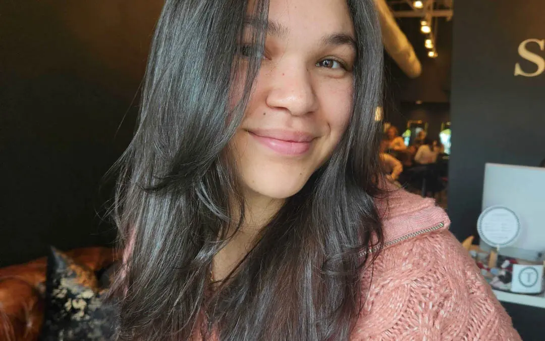 Close-up portrait of a smiling woman showing off a fresh haircut of long, glossy dark brown hair with distinct face-framing layers and internal texturizing, expertly styled with a polished blowout at Sunday Salon in Raleigh.
