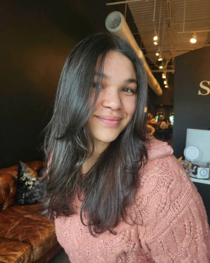 Glossy Dark Haircut with Long Face-Framing Layers Close-up portrait of a smiling woman showing off a fresh haircut of long, glossy dark brown hair with distinct face-framing layers and internal texturizing, expertly styled with a polished blowout at Sunday Salon in Raleigh.