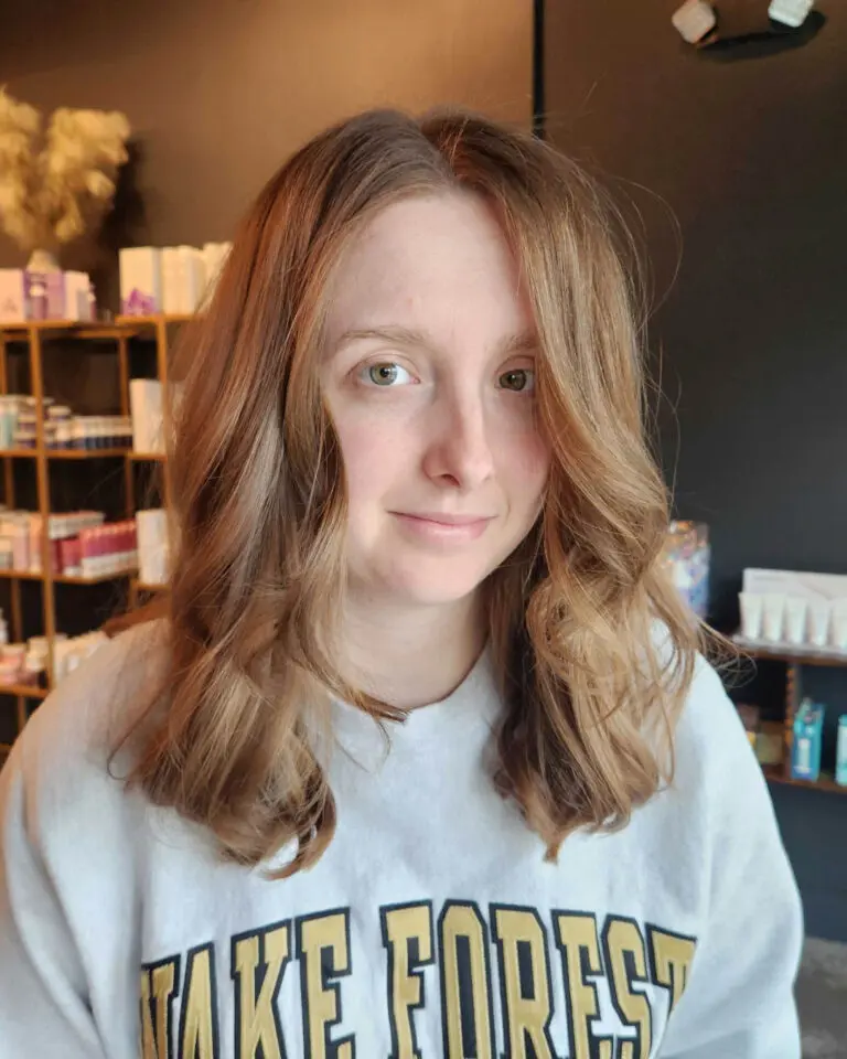 Client showcasing a mid-length haircut with warm strawberry blonde and light copper tones, featuring soft face-framing waves styled perfectly at Sunday Salon in Raleigh.