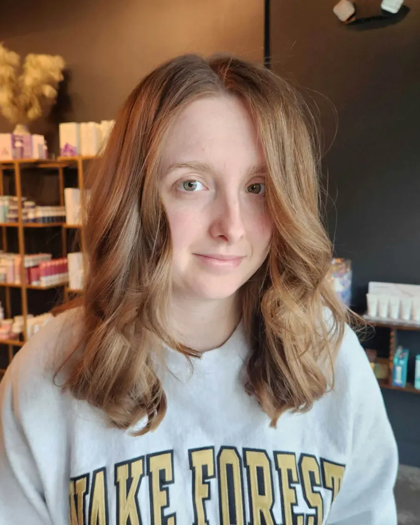 Warm Strawberry Blonde Lob with Soft Voluminous Waves Client showcasing a mid-length haircut with warm strawberry blonde and light copper tones, featuring soft face-framing waves styled perfectly at Sunday Salon in Raleigh.