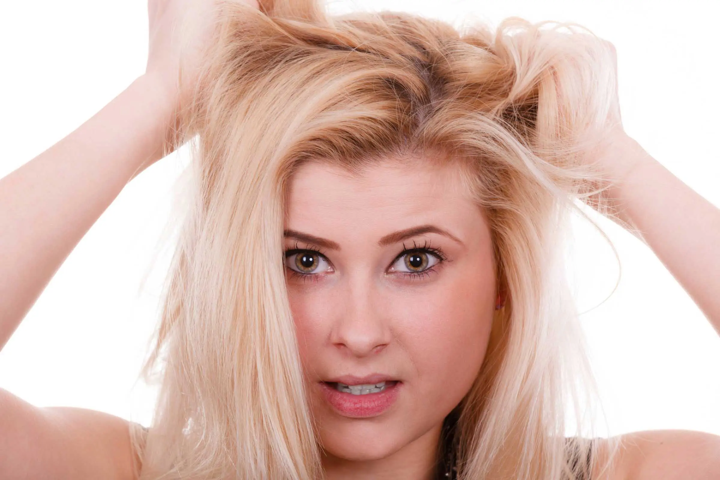 A young person with long blonde hair appears frustrated, holding their hair with both hands. The background is plain white, and they are looking directly at the camera with a concerned expression. Perhaps a visit to one of the best hair salons in Cary, NC is in order!