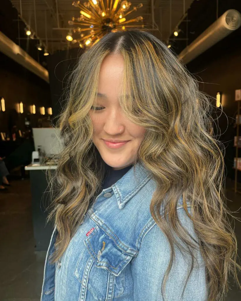 Front-facing view of a smiling client featuring long wavy brunette hair with warm golden caramel balayage and face-framing highlights at Sunday Salon in Raleigh.