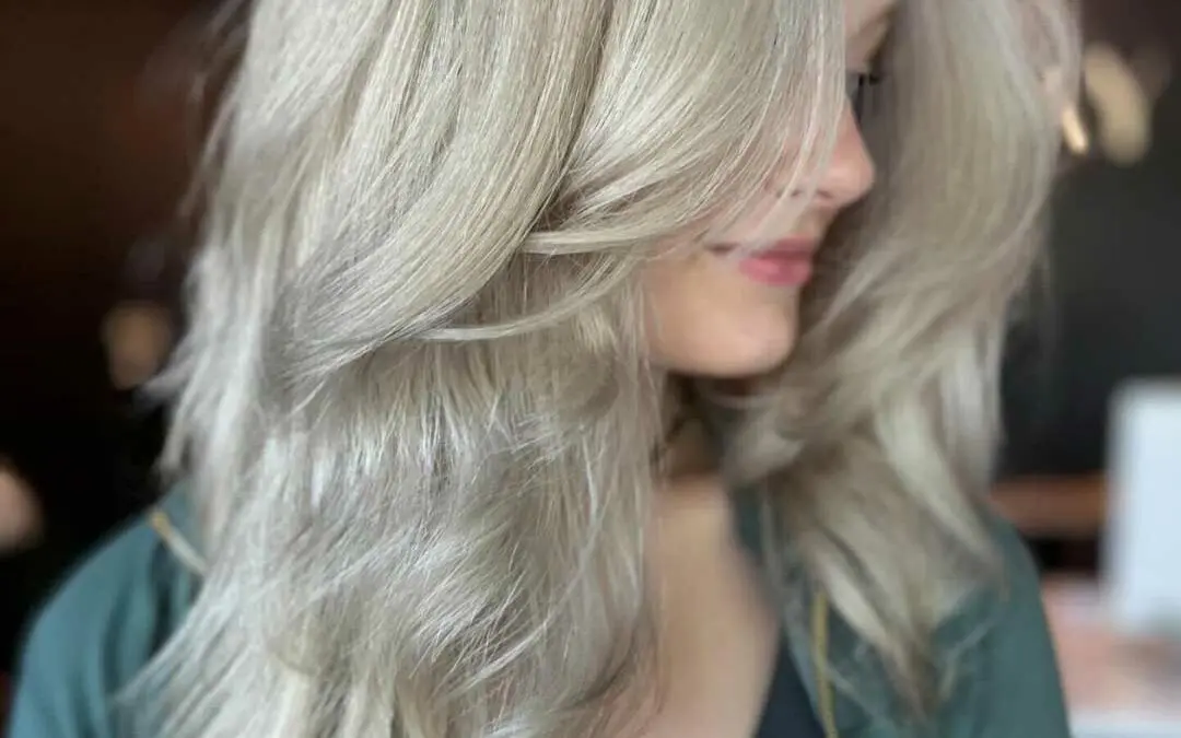Profile view of a client with mid-length hair featuring a pristine icy platinum blonde color and a voluminous blowout with sweeping face-framing layers, styled at Sunday Salon in Raleigh.