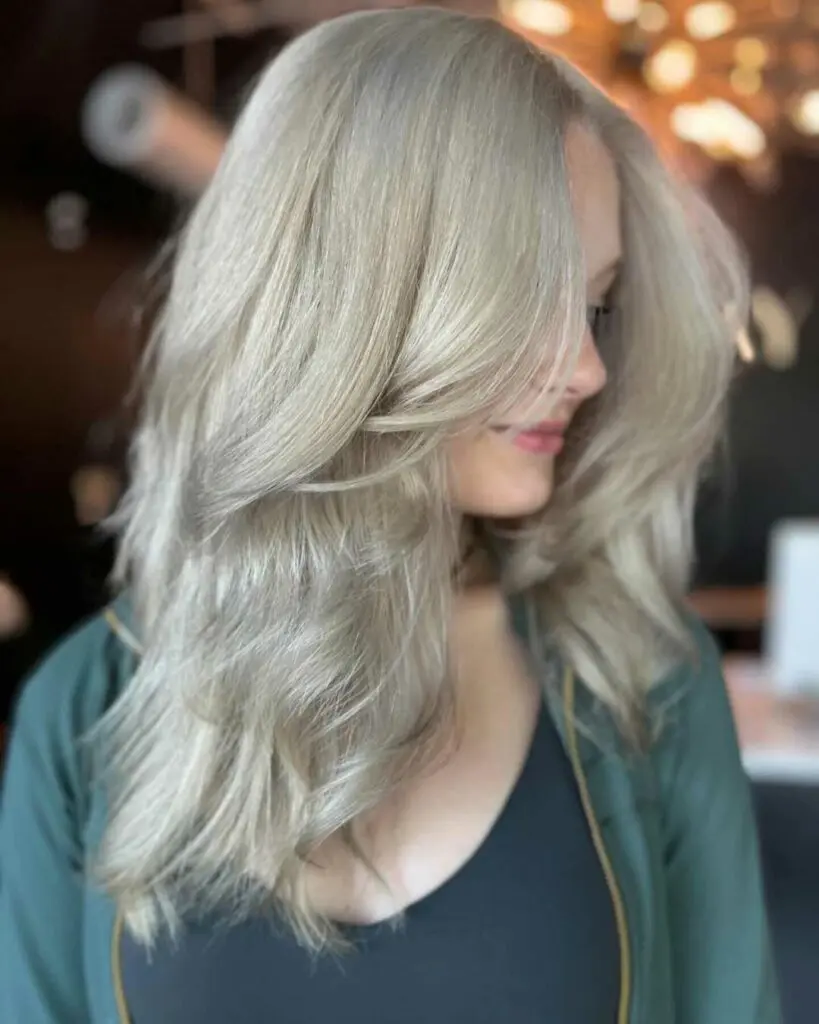 Icy Platinum Blonde with Voluminous Face-Framing Blowout Profile view of a client with mid-length hair featuring a pristine icy platinum blonde color and a voluminous blowout with sweeping face-framing layers, styled at Sunday Salon in Raleigh.