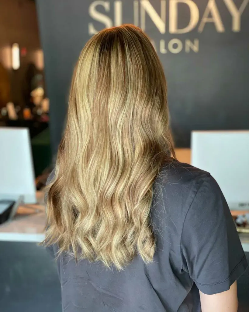 Dimensional Honey Blonde Highlights and Soft Layered Cut on Long Waves Back view of a client with long wavy hair featuring dimensional honey blonde highlights and a fresh, soft layered haircut at Sunday Salon in Raleigh.