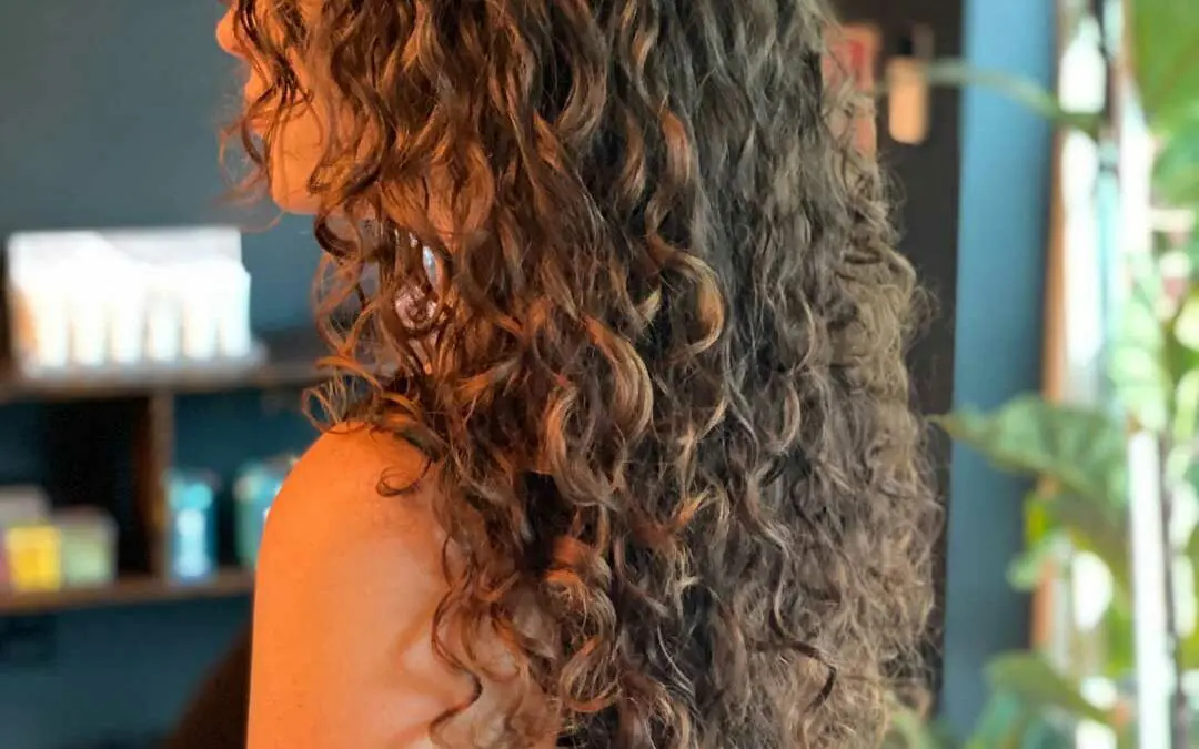 Side profile of a client with long, naturally curly brunette hair featuring defined ringlets, custom layers, and a soft curly fringe styled at Sunday Salon in Raleigh.