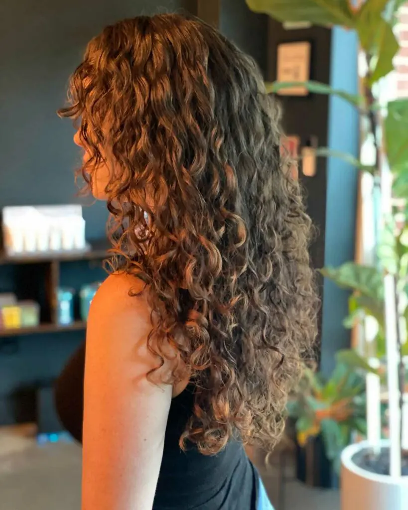 Long Defined Brunette Curls with Custom Layering and Face-Framing Fringe Side profile of a client with long, naturally curly brunette hair featuring defined ringlets, custom layers, and a soft curly fringe styled at Sunday Salon in Raleigh.