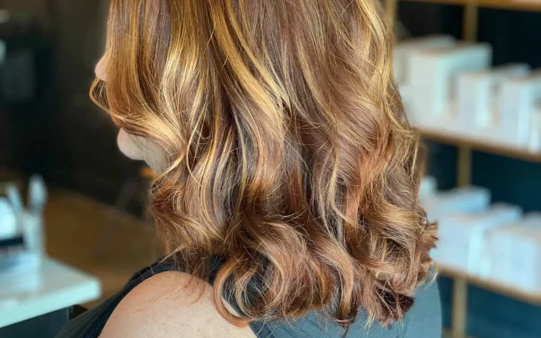 Mid-length warm auburn hair featuring vibrant golden copper highlights and bouncy curls, expertly colored and styled at Sunday Salon in Raleigh.