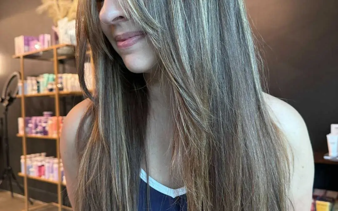 A beautiful client at Sunday Salon in Raleigh showcasing an ultra-long, sleek straight haircut with face-framing layers and curtain bangs, beautifully illuminated by dimensional ash blonde highlights over a dark brunette base.