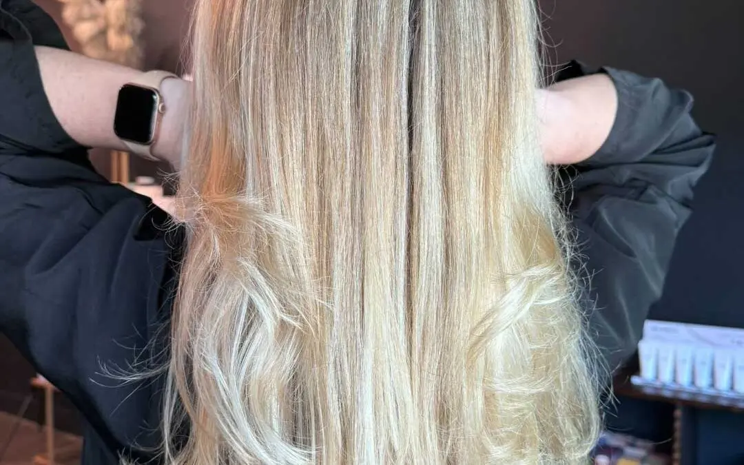 Back view of a client at Sunday Salon in Raleigh showcasing mid-back length bright vanilla blonde hair with dimensional highlights, styled in a voluminous, bouncy layered blowout with flipped ends.