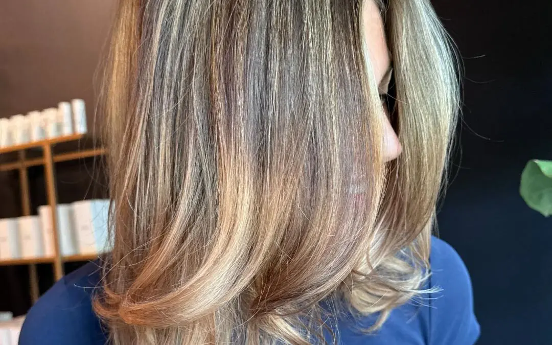 Mid-length brown hair with dimensional honey and ash blonde highlights, styled in a sleek, bouncy layered blowout with flipped ends at Sunday Salon in Raleigh.