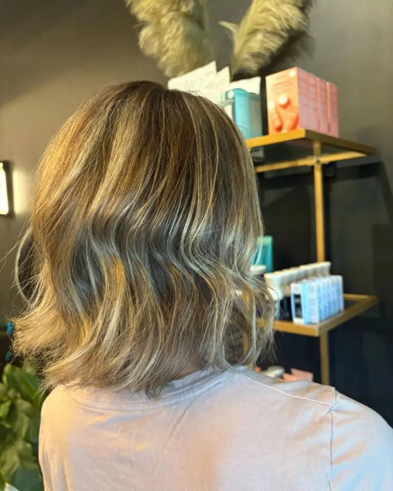 Back view of a client at Sunday Salon in Raleigh showcasing a stylish, shoulder-length textured bob styled with effortless beachy waves, featuring bright sun-kissed golden blonde highlights.