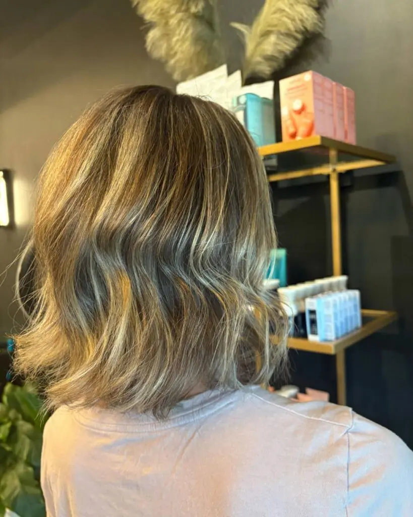 Sun-Kissed Golden Blonde Textured Bob Back view of a client at Sunday Salon in Raleigh showcasing a stylish, shoulder-length textured bob styled with effortless beachy waves, featuring bright sun-kissed golden blonde highlights.