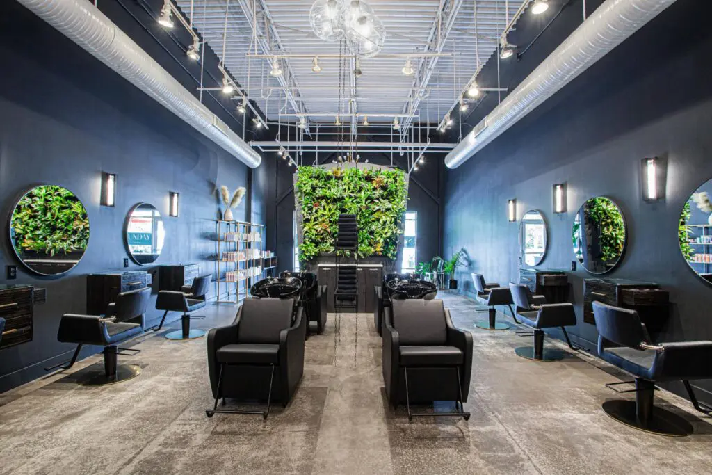 award winning salon Modern, award winning salon with black chairs, round mirrors, and wall-mounted plants. The space features high ceilings, exposed ducts, bright lighting, and a large green plant wall at the back for a stylish, inviting atmosphere.