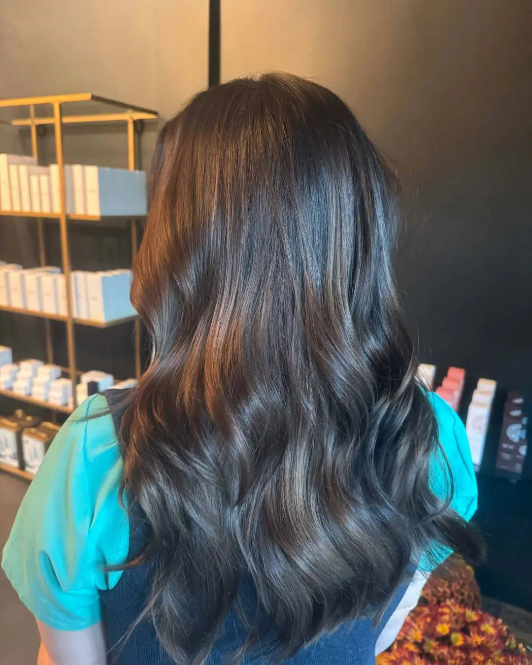 A client with long, beautifully glossy espresso brown hair featuring delicate caramel ribbons and styled in smooth, polished waves, created at Sunday Salon in Raleigh.