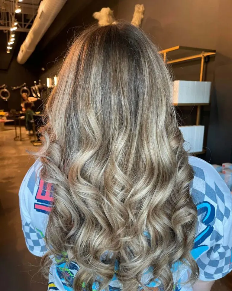 The back of a client's head at Sunday Salon in Raleigh, showcasing long, thick hair with multidimensional cool ash blonde highlights. The hair is styled smooth at the crown and cascades into beautifully defined, bouncy curls at the ends, highlighting the seamless blend and high-shine finish.