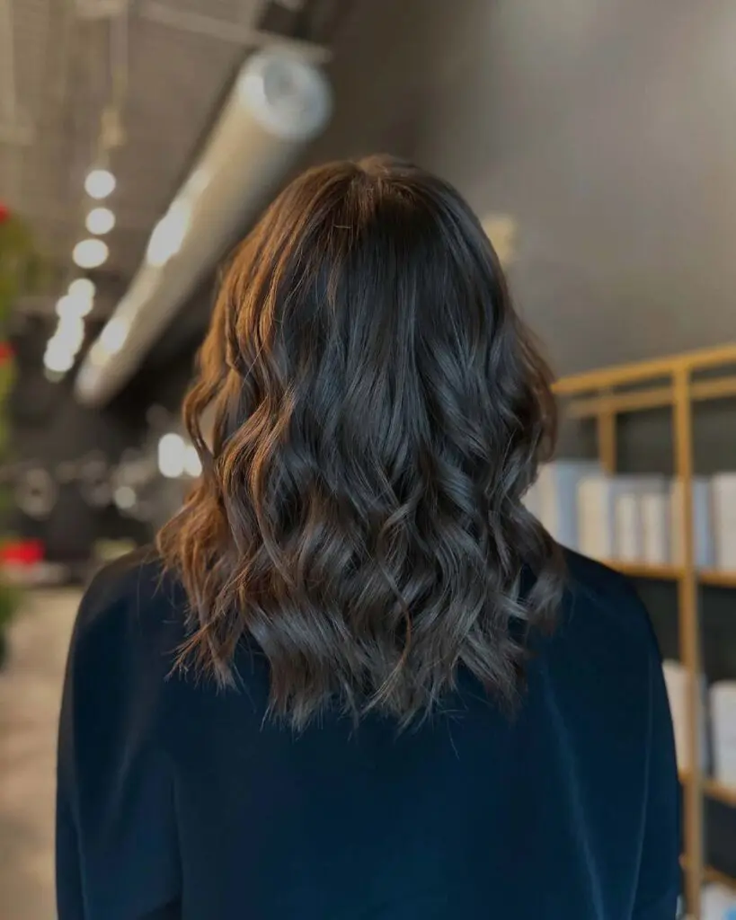 A client with a mid-length dark chocolate brunette lob styled in a voluminous blowout with bouncy, defined waves and incredible shine at Sunday Salon in Raleigh.