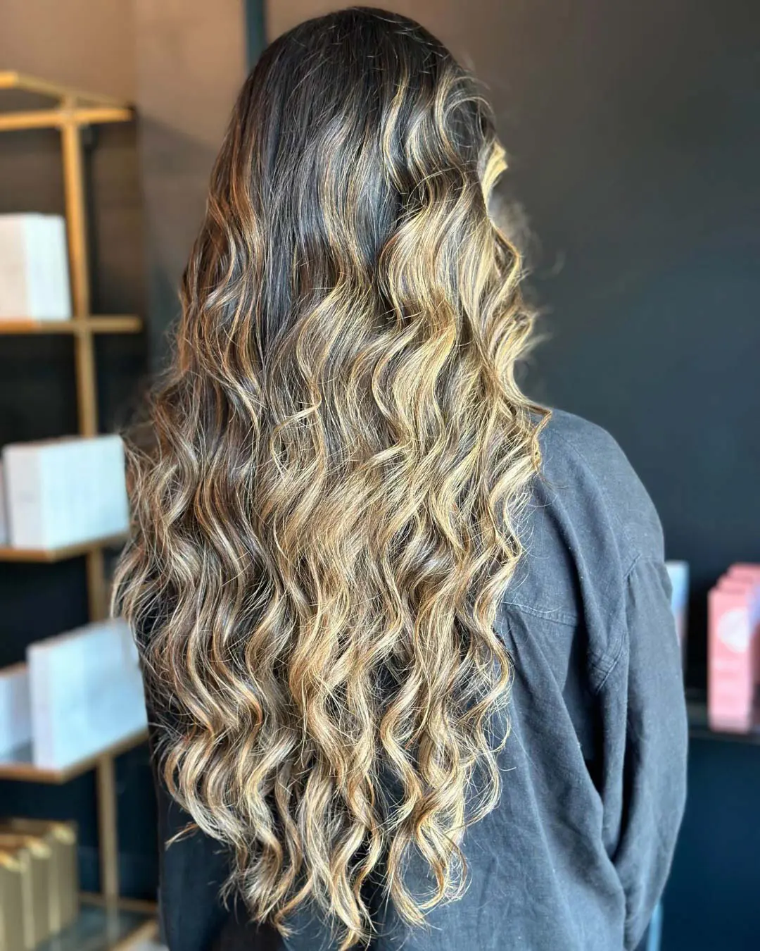 A client showcasing ultra-long hair styled in a voluminous, wavy blowout with high-contrast golden blonde dimensional highlights, beautifully crafted at Sunday Salon in Raleigh.