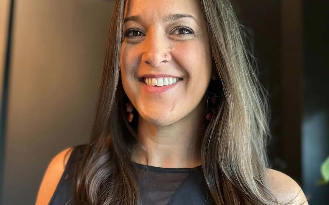 A smiling client showcasing a polished, long brunette blowout with subtle ash face-framing dimension and softly curled ends, created at Sunday Salon in Raleigh.