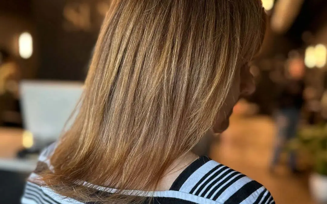 A client showcasing shoulder-length hair styled in a sleek and smooth blowout, featuring dimensional warm honey blonde highlights, created at Sunday Salon in Raleigh.