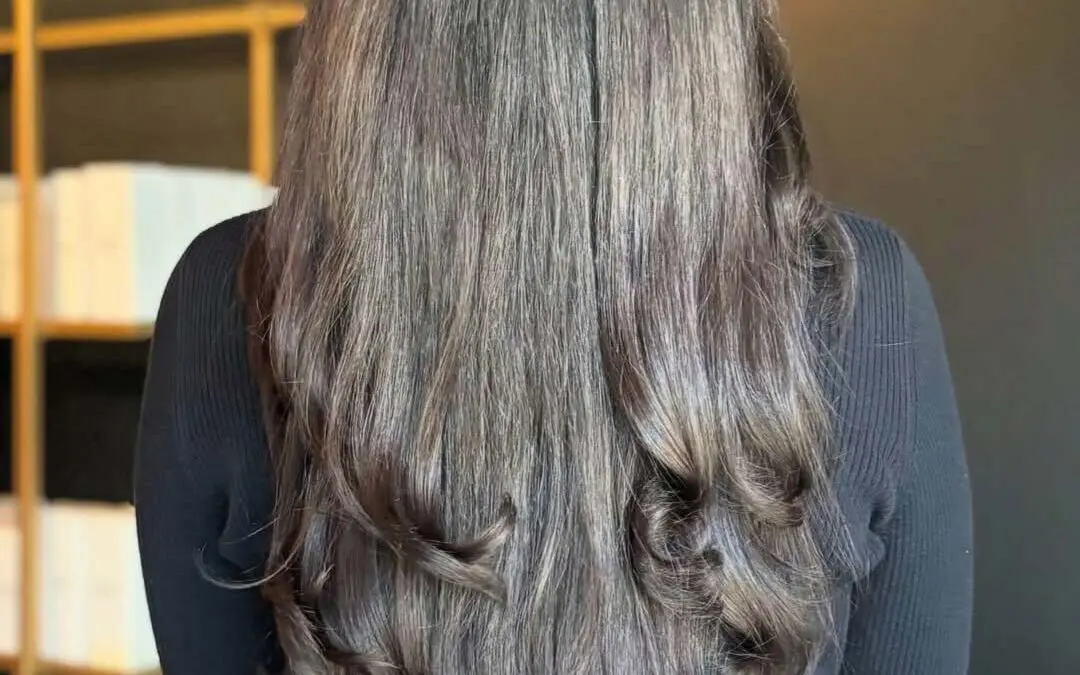 A client showcasing ultra-long, thick mocha brunette hair styled smooth at the roots with voluminous bouncy curls at the ends, created at Sunday Salon in Raleigh.