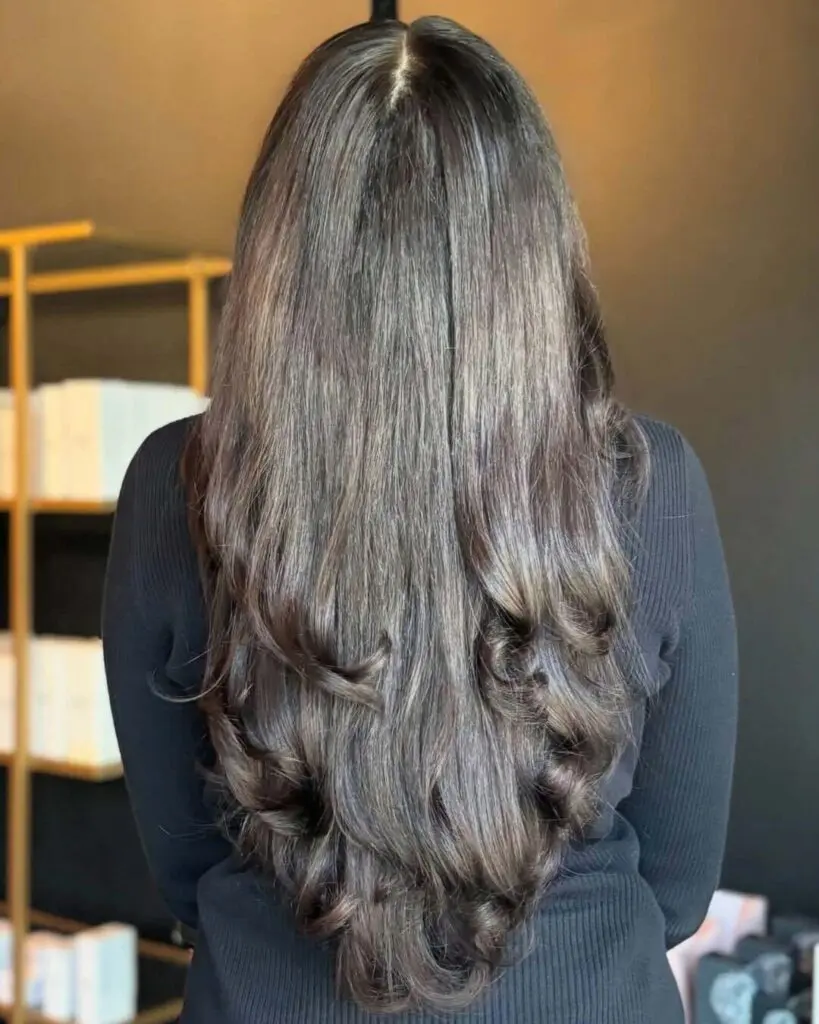 Ultra-Long Mocha Brunette with Voluminous Layered Ends A client showcasing ultra-long, thick mocha brunette hair styled smooth at the roots with voluminous bouncy curls at the ends, created at Sunday Salon in Raleigh.