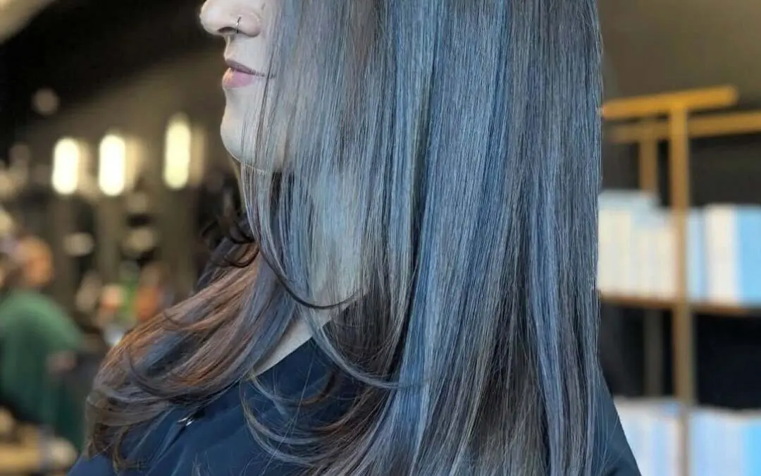 A side profile of a client with long, sleek dark cool-toned brunette hair featuring smooth face-framing layers and gently beveled ends, styled at Sunday Salon in Raleigh.