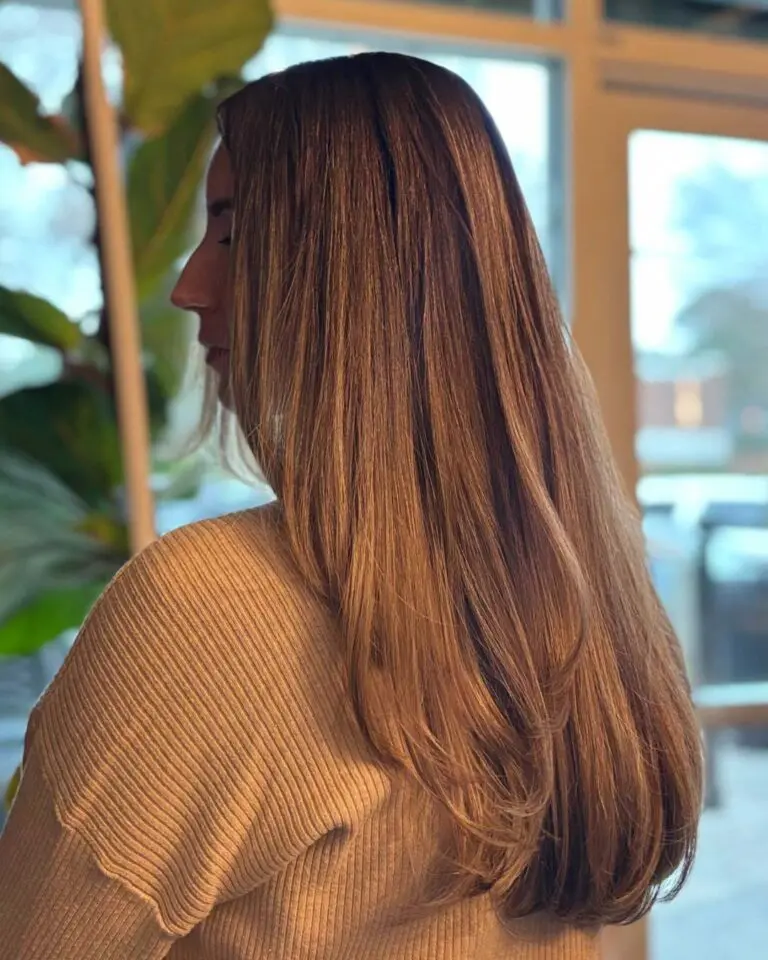 A side profile of a client showing off ultra-long, thick, warm caramel brunette hair styled in a sleek blowout with softly sweeping layered ends at Sunday Salon in Raleigh.