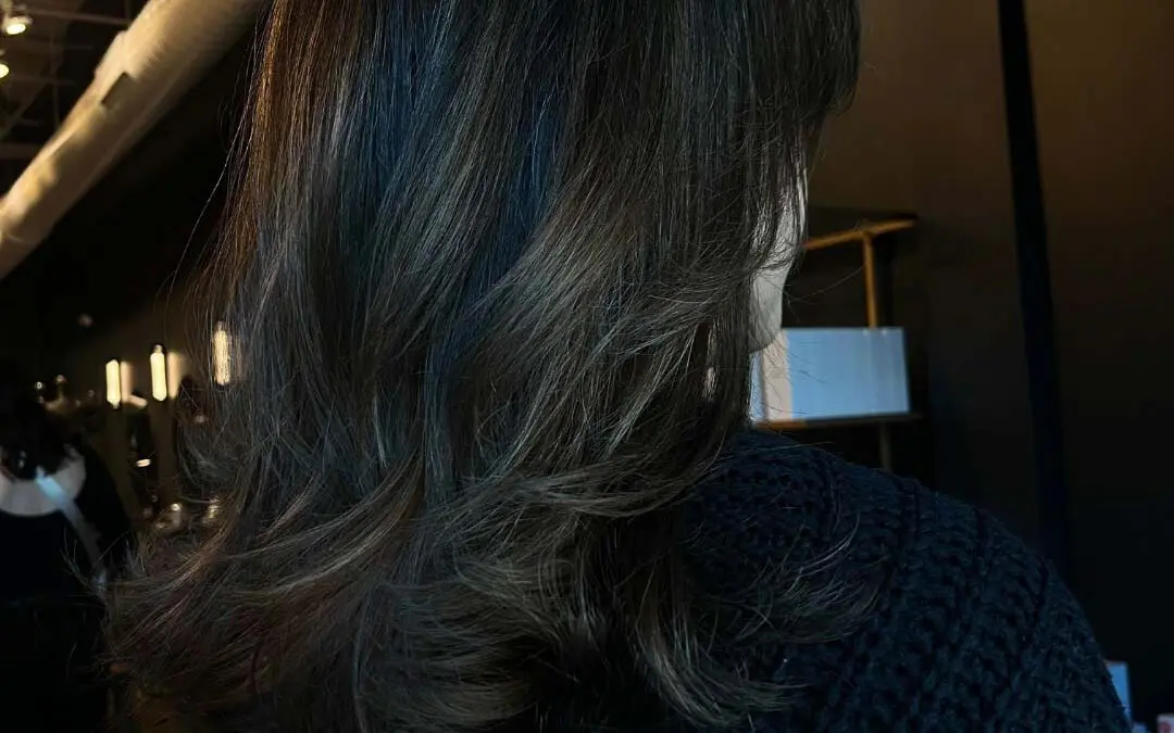 A client showcasing a sophisticated mid-length deep espresso brunette haircut styled with a smooth blowout and sweeping layered ends at Sunday Salon in Raleigh.