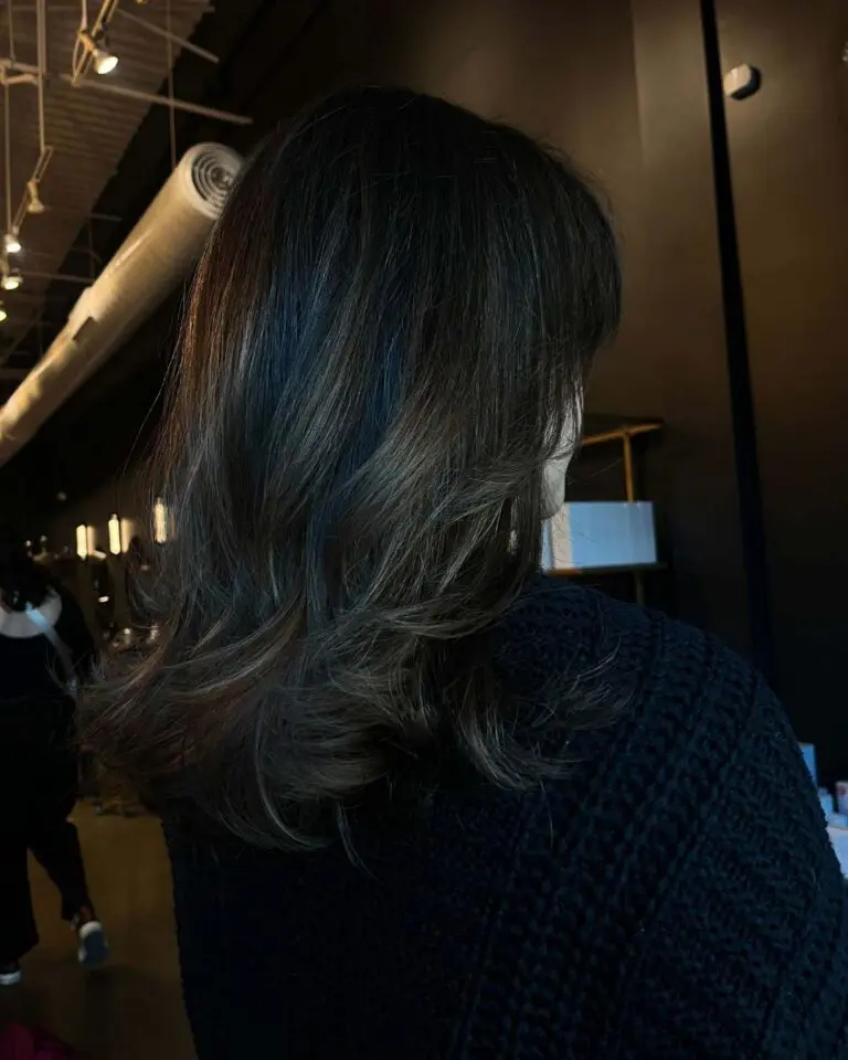 A client showcasing a sophisticated mid-length deep espresso brunette haircut styled with a smooth blowout and sweeping layered ends at Sunday Salon in Raleigh.