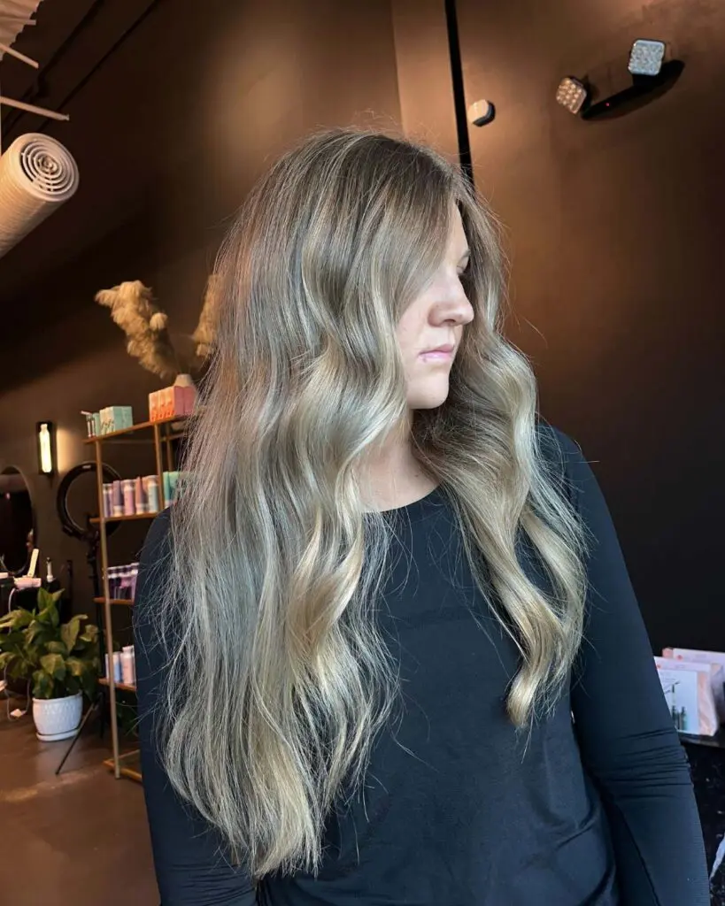 A client showcasing an ultra-long layered haircut featuring a seamless cool-toned ash blonde balayage and effortless soft waves, created at Sunday Salon in Raleigh.