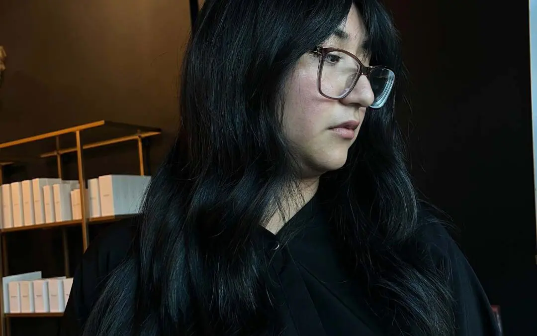 A client showcasing long, glossy jet black hair styled in loose waves with soft, face-framing curtain bangs, expertly cut and colored at Sunday Salon in Raleigh.
