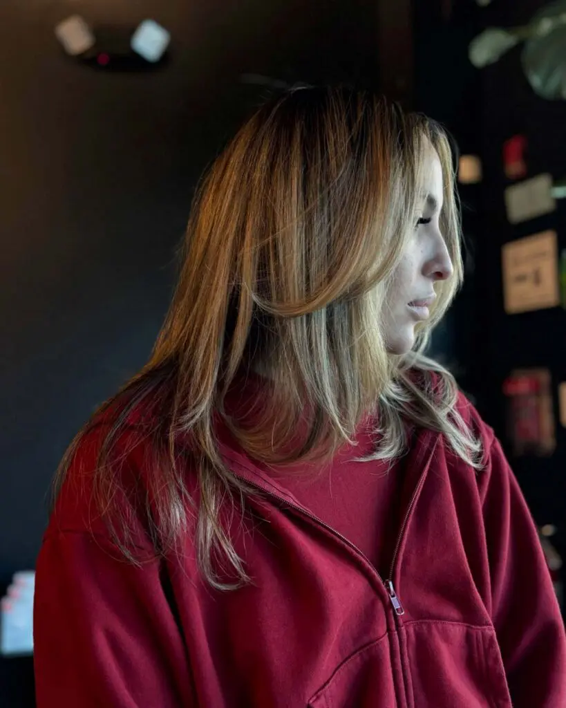 Jada_Handy_Portfolio_6 A side profile of a client with mid-length warm honey blonde highlighted hair, styled in a smooth blowout with sweeping face-framing layers at Sunday Salon in Raleigh.